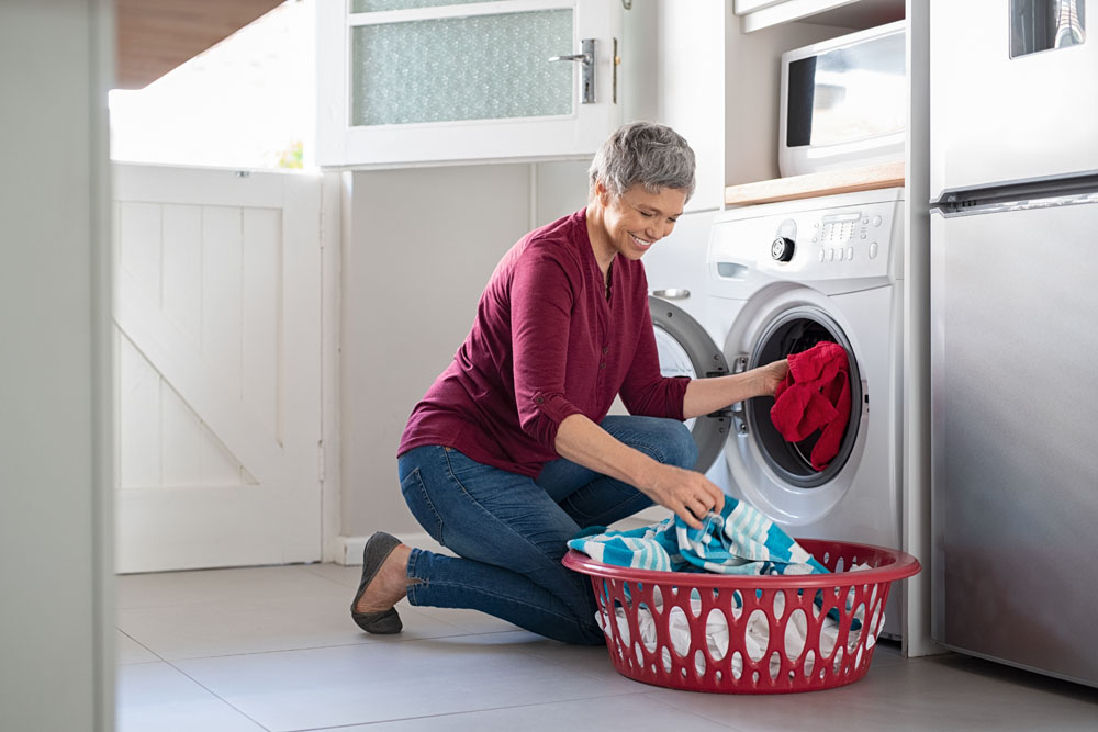 happy,senior,woman,loading,dirty,clothes,in,washing,machine.,smiling