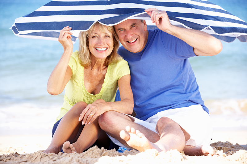senior,couple,sheltering,from,sun,under,beach,umbrella