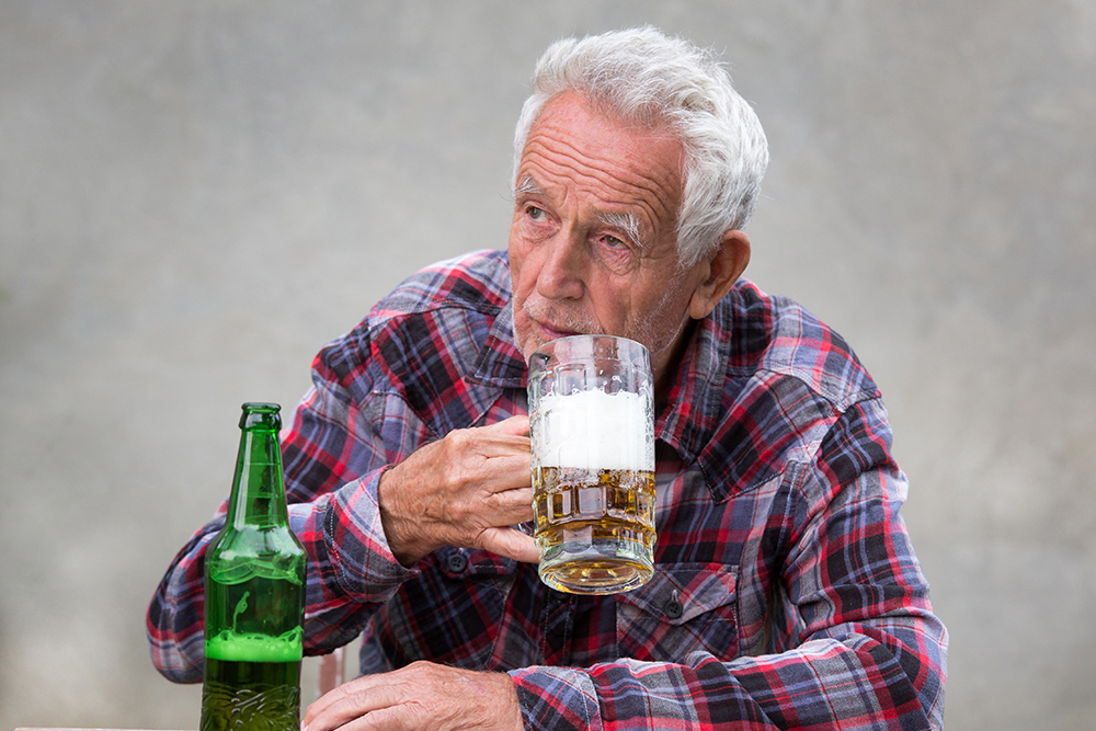 senior,man,sitting,at,table,and,drinking,beer,from,mug