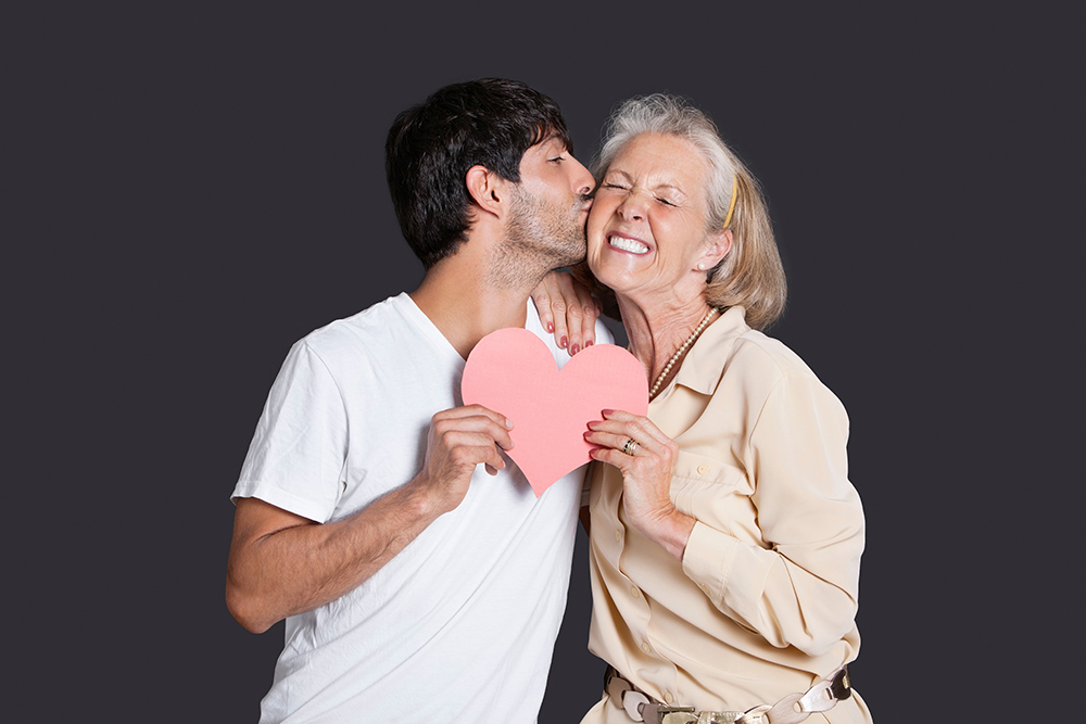 young,man,kissing,senior,woman,with,red,paper,heart,against