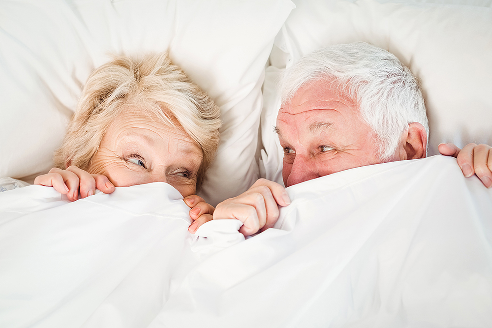 overhead,view,of,senior,couple,hiding,in,blanket,on,bed