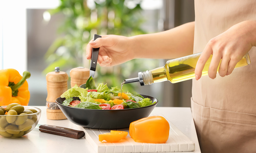 woman,dressing,fresh,vegetable,salad,with,olive,oil,in,kitchen