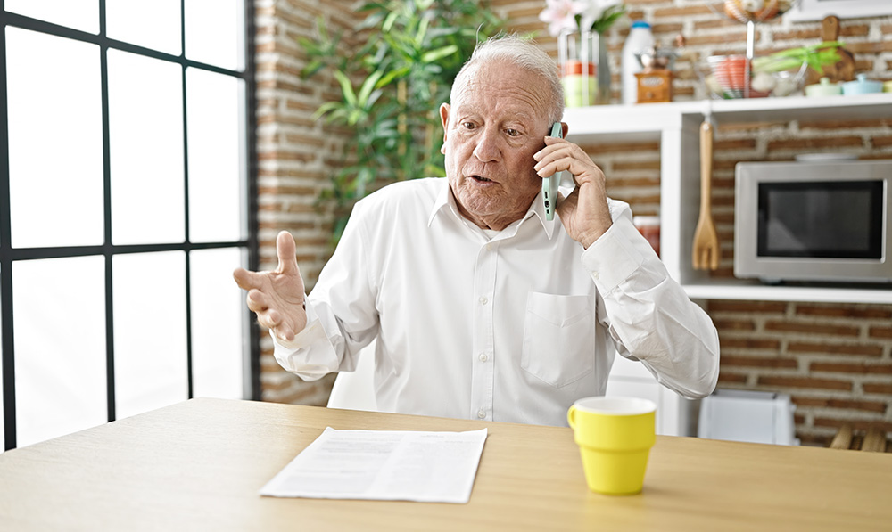 senior,grey haired,man,angry,arguing,on,smartphone,sitting,on,table