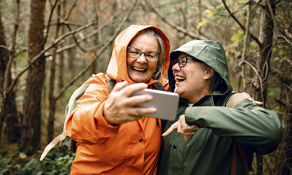 senior,women,friends,laughing,together,on,forest,hike,in,raincoats