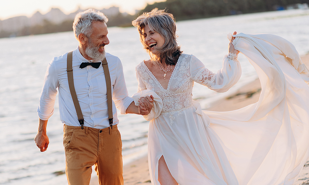 cheerful,elderly,couple,runs,along,beach,holding,hands.