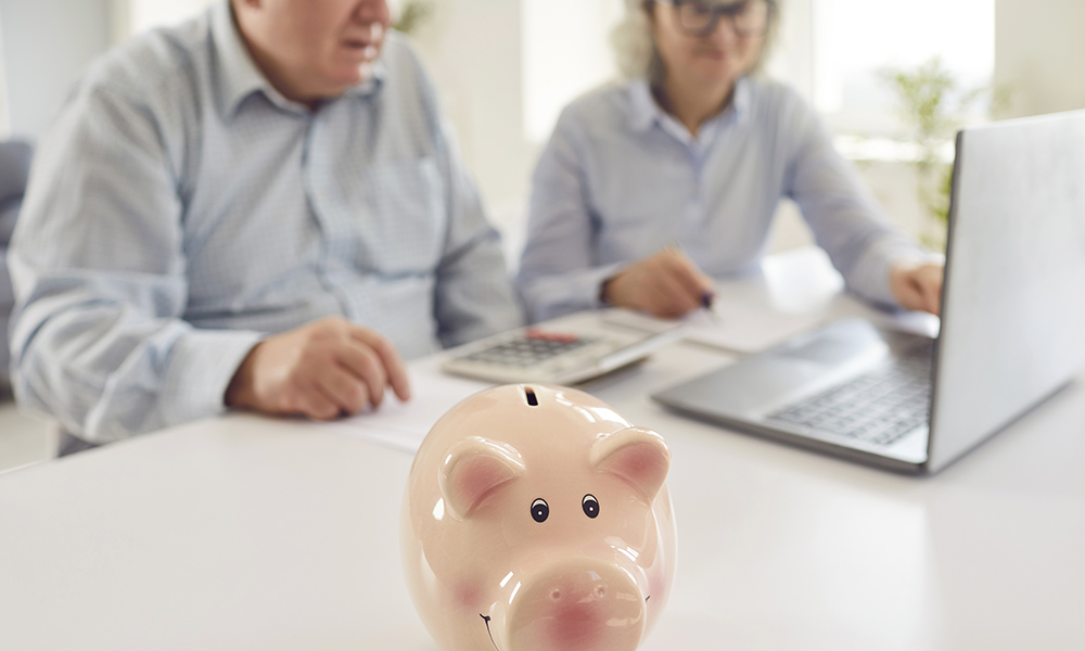 senior,couple,sitting,at,table,with,piggy,bank,and,calculating