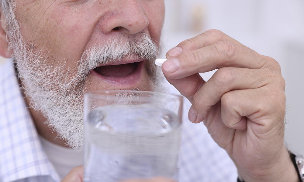 senior,man,with,glass,of,water,taking,pill,at,home,