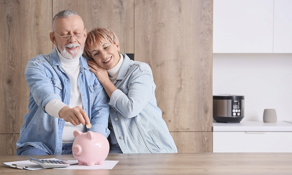 mature,couple,putting,coin,into,piggy,bank,in,kitchen