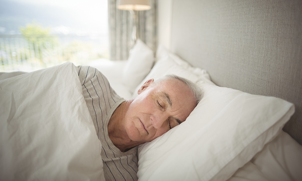 senior,man,sleeping,under,white,duvet,in,bedroom,beside,sliding