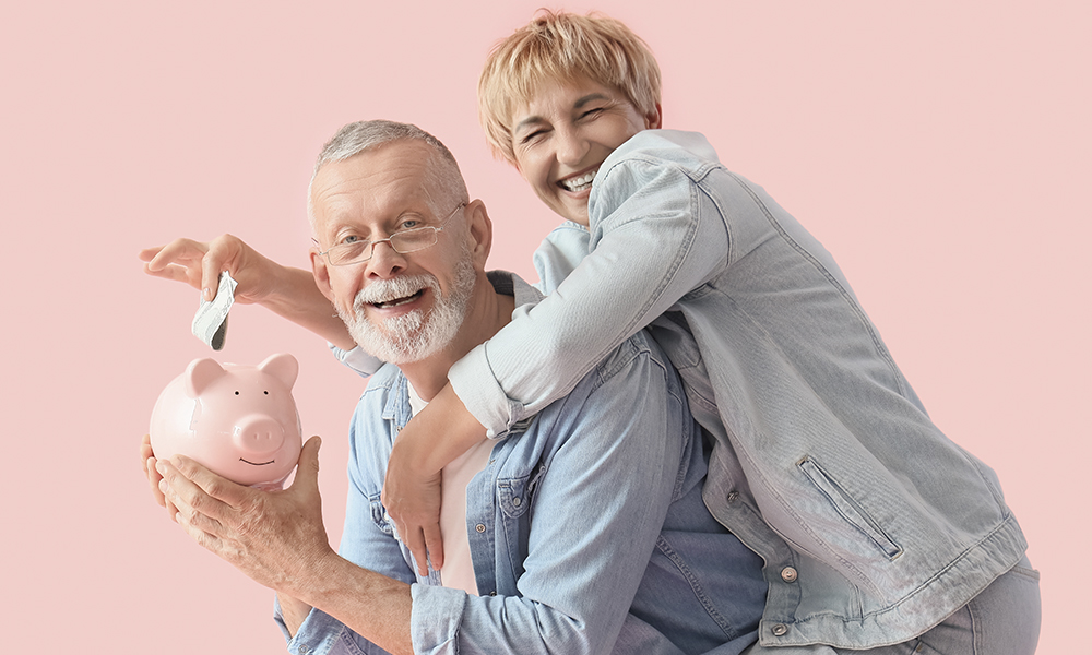 happy,mature,couple,putting,money,into,piggy,bank,on,pink